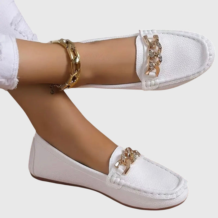 White slip-on loafers with gold chain ornament on the vamp and textured upper.
