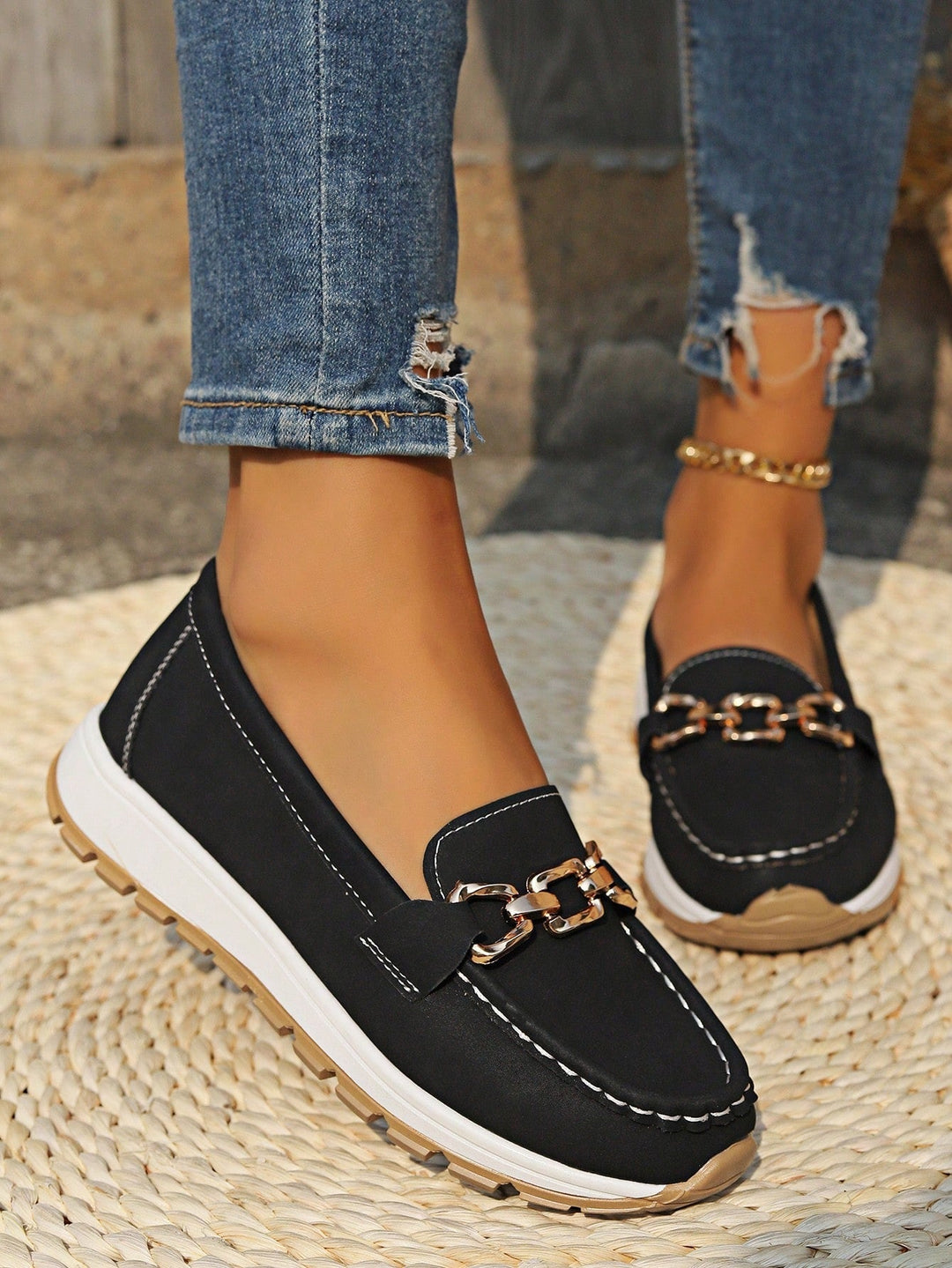 Black slip-on loafers with gold chain bar detail and white midsole with textured tread.