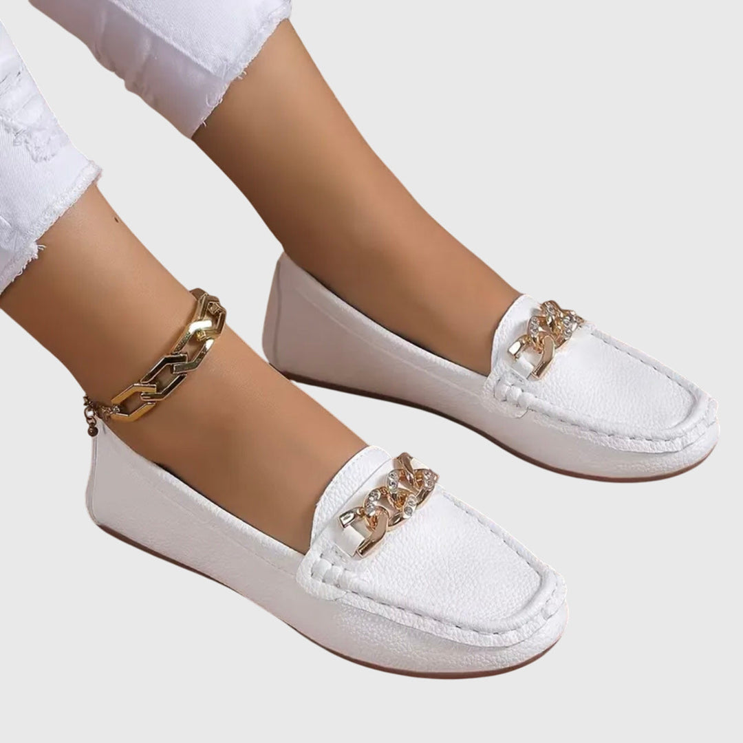 White slip-on loafers with gold chain detail across the front and stitched moc toe.