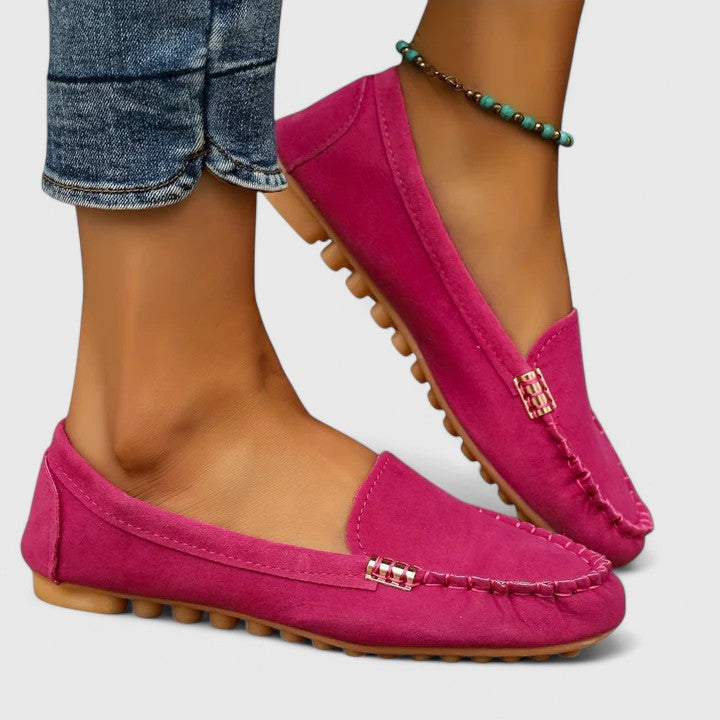Pink suede slip-on loafers with metal buckle accent and rubber sole tread