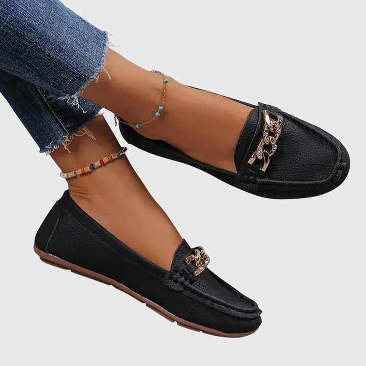 Black slip-on loafers with gold chain detail on the vamp and stitched moc-toe design.