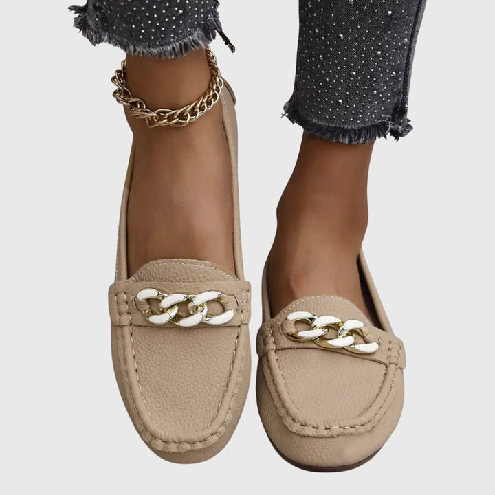 Beige slip-on loafers with gold chain-ornament detail on the vamp and stitched edges.