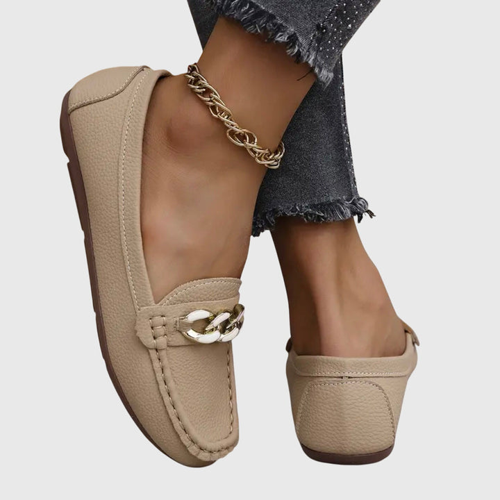 Beige slip-on loafers with gold chain detail on the vamp and stitched moc-toe design.