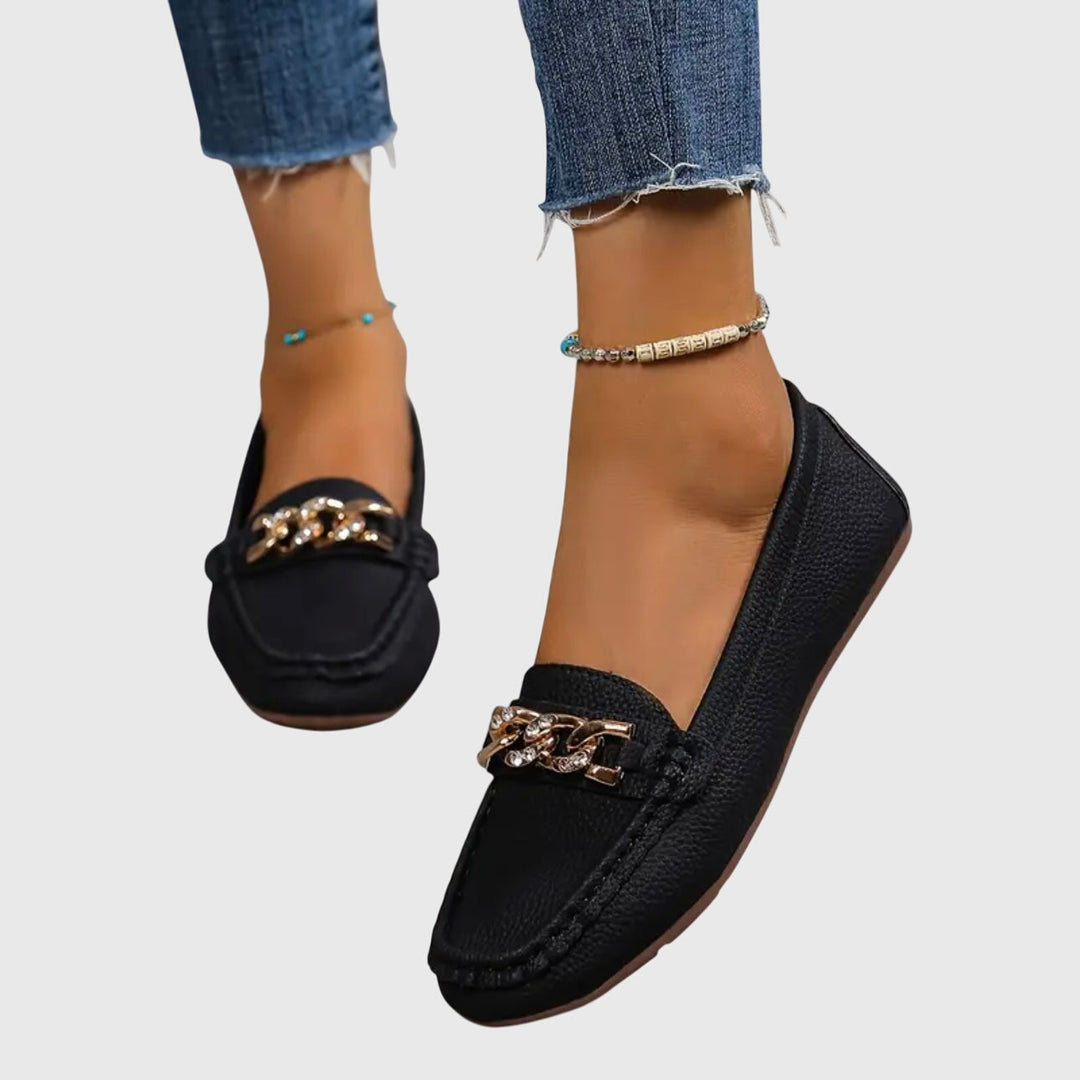 Black slip-on loafers with gold chain ornament on the vamp and smooth moc-toe stitching.
