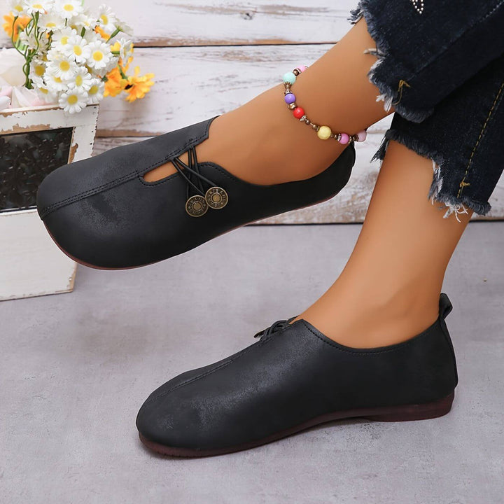 Black slip-on flats with button detail and rounded toe; side view on foot