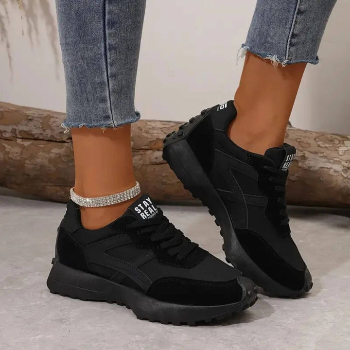Black lace-up trainers with thick tread sole and 'STAY REAL' heel tab