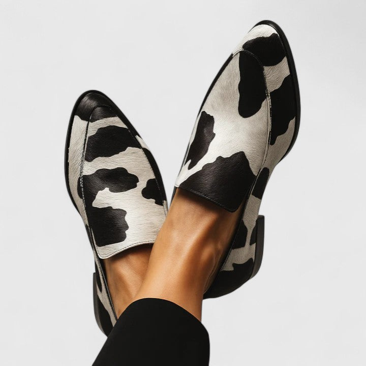 Black-and-white cow print slip-on loafers, side view with sculpted heel and black lining