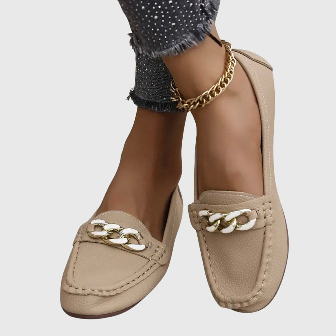 Beige slip-on loafers with gold chain ornament on the front and low-profile sole.