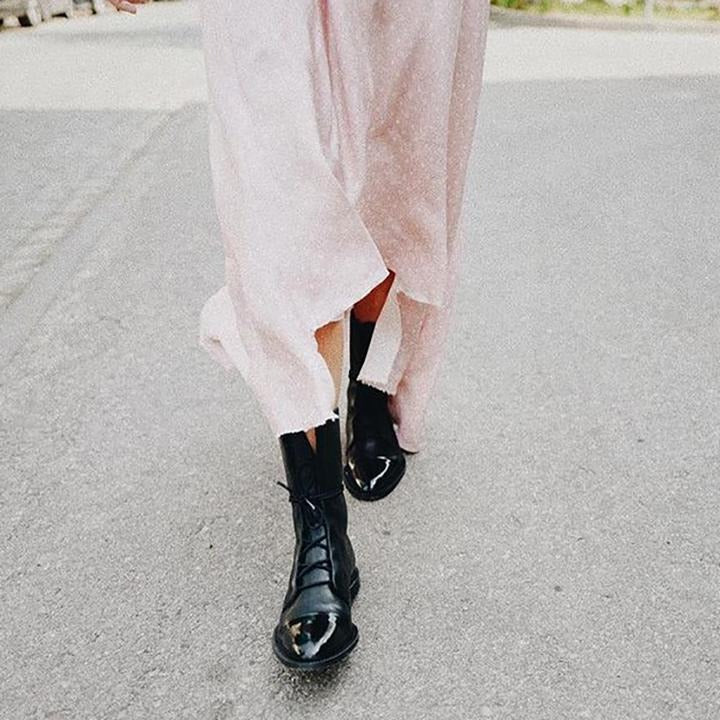 Black lace-up ankle boots with glossy toe and crisscross laces under light pants.
