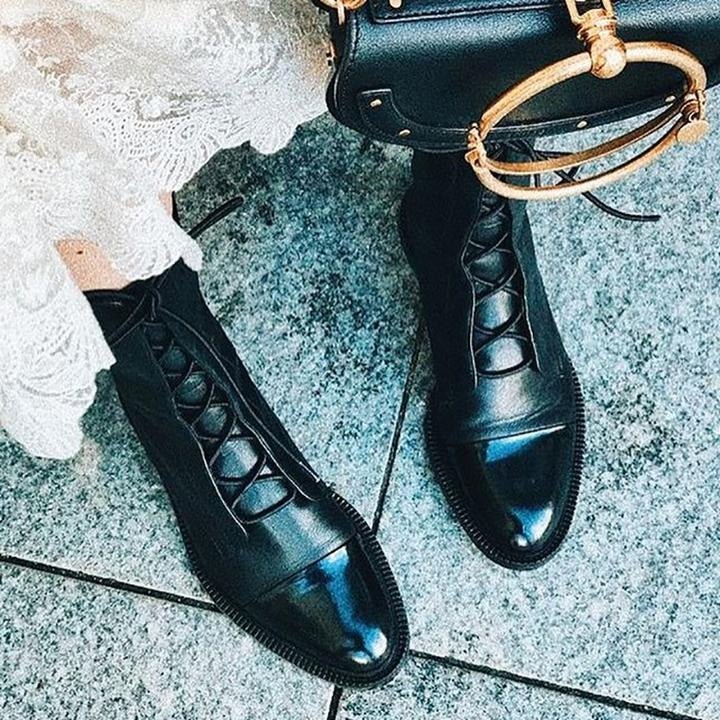Black lace-up ankle boots with side laces and rounded toe, styled with skirt.