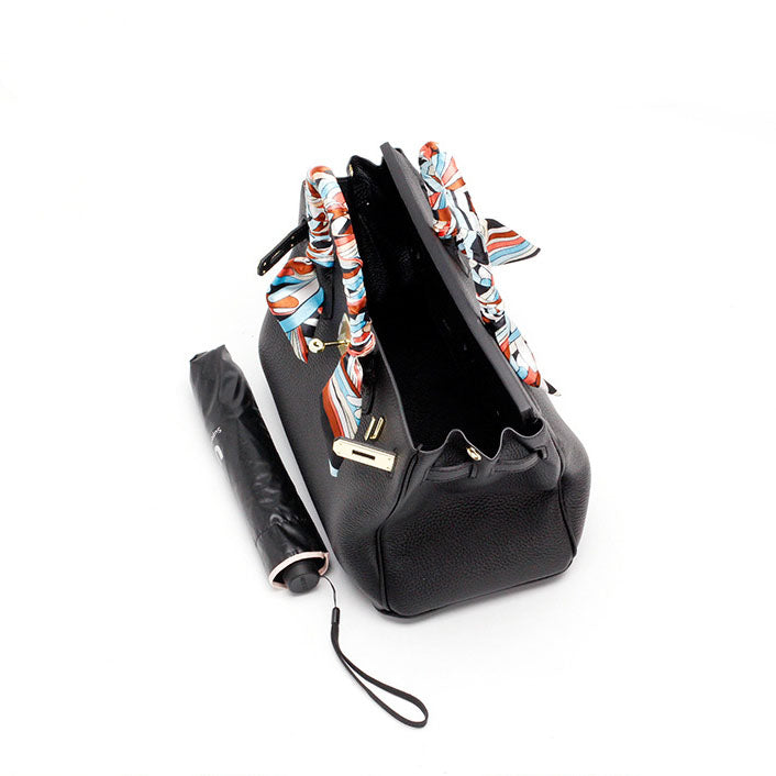 Black handbag with front flap, colorful patterned scarf handle, and chain strap