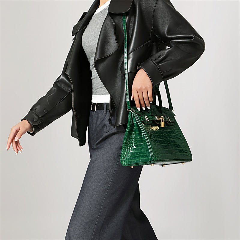Green croc-embossed handbag with gold latch, held by model.