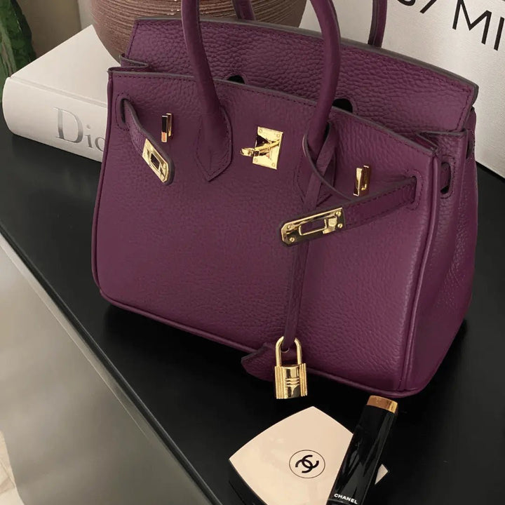 Purple leather handbag with top handles, front flap, and gold-tone hardware.