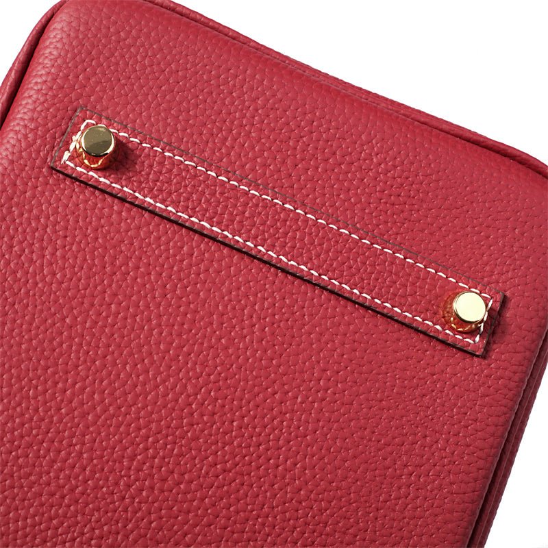Wine red leather handbag side pocket with stitched trim and gold button hardware.