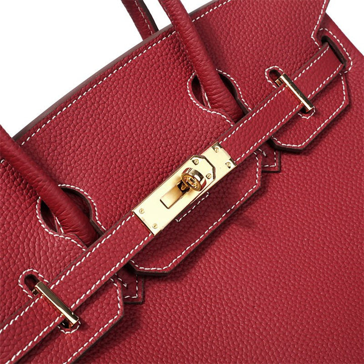 Wine red leather handbag strap and metal clasp detail with gold hardware and stitching.
