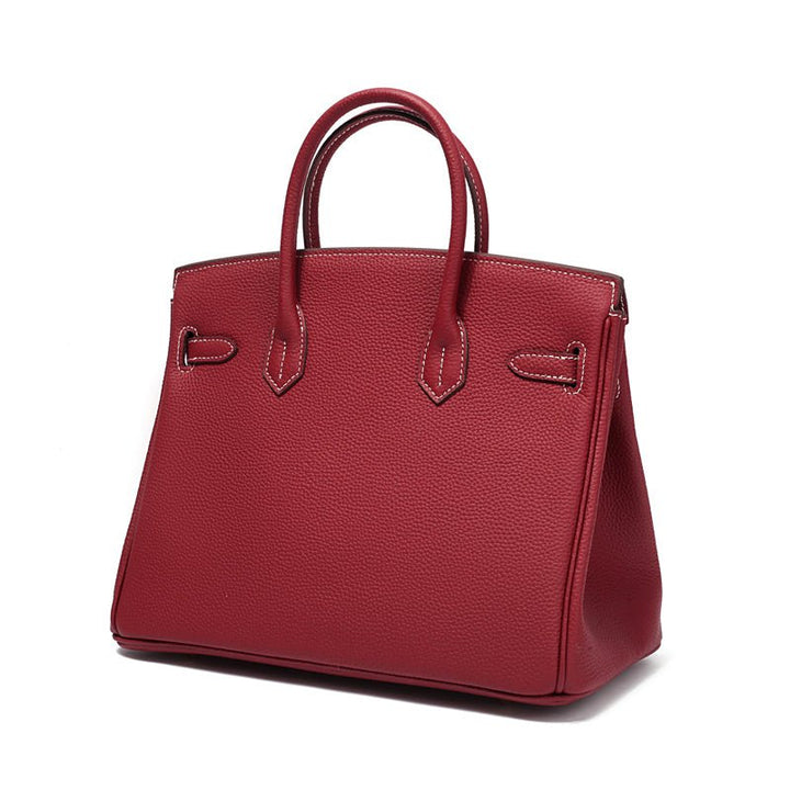 Wine red leather handbag with top handles and decorative front straps, gold hardware.