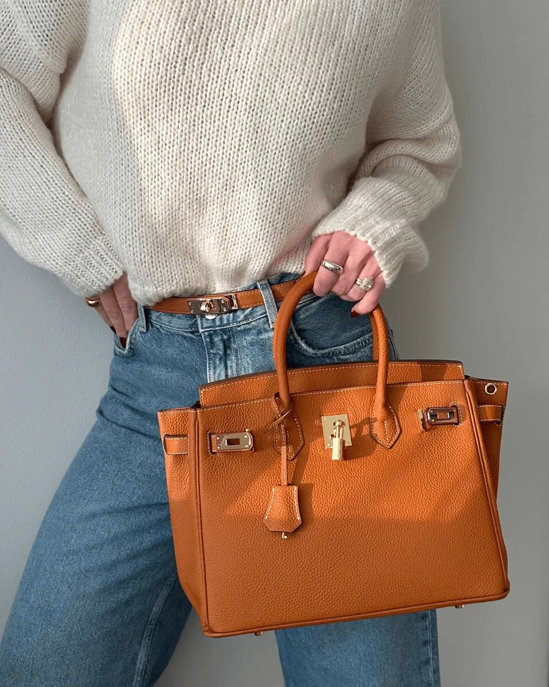 Women’s handbag with top handles, front lock detail, and gold hardware in orange.